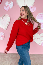 Load image into Gallery viewer, Woman wearing a red sweater and blue jeans with a pink heart-themed background