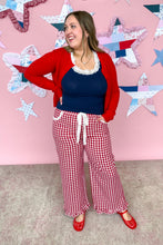 Load image into Gallery viewer, Woman wearing a red cardigan, blue top, and red checkered pants against a pink wall with star patterns.