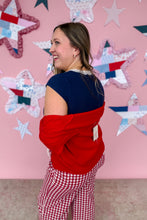 Load image into Gallery viewer, Woman wearing a red and navy sweater with a pink star-patterned wall in the background
