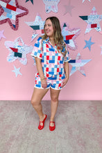 Load image into Gallery viewer, Woman in a colorful checkered outfit standing in front of a pink wall with star-shaped decorations.