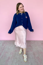 Load image into Gallery viewer, Woman wearing a blue cardigan and pink skirt standing against a pink wall.