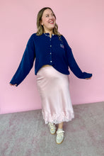 Load image into Gallery viewer, Woman wearing a blue cardigan and pink satin skirt against a pink wall.