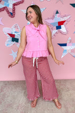 Load image into Gallery viewer, Woman wearing a pink sleeveless top with a bow and red checkered pants against a pink wall with star decorations.