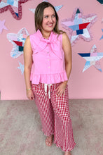Load image into Gallery viewer, Woman wearing a pink top and red checkered pants standing in front of a decorative wall with star patterns.