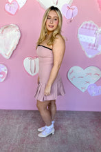 Load image into Gallery viewer, Woman in a pink pleated dress standing in front of a heart-patterned wall side view