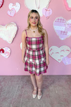 Load image into Gallery viewer, Woman in a plaid dress standing in front of a pink wall with heart decorations