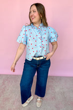 Load image into Gallery viewer, Girl wearing a blue top with red polkadots with puff sleeves and dark wash jeans standing in front of a pink background.