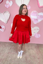 Load image into Gallery viewer, Woman wearing a red sweater with a heart design over a red dress in front of a pink wall with heart decorations.