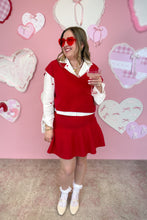 Load image into Gallery viewer, Woman in a red skirt set with heart-shaped sunglasses standing in front of a heart-themed wall.