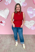 Load image into Gallery viewer, Woman in a red sleeveless top and blue jeans standing in front of a pink wall with heart decorations.