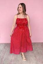 Load image into Gallery viewer, A woman modeling a red and white vertically striped midi dress with a smocked bodice, and beige strappy heels, set against a solid pink studio background.