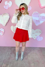 Load image into Gallery viewer, Woman in a white blouse, red skirt, and silver boots standing in front of a pink wall with heart decorations.