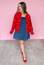 Load image into Gallery viewer, Woman wearing a red cardigan with white stars over a blue dress against a pink background