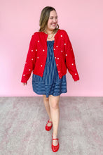Load image into Gallery viewer, Woman wearing a red star cardigan, blue dress, and red shoes against a pink background