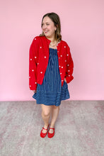Load image into Gallery viewer, Woman wearing a red star cardigan, blue dress, and red shoes against a pink background
