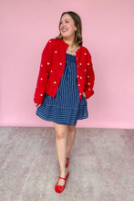 Load image into Gallery viewer, Woman wearing a red star cardigan, blue dress, and red shoes against a pink background