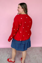 Load image into Gallery viewer, Woman wearing a red cardigan with white stars and a blue striped dress against a pink background