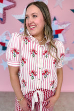 Load image into Gallery viewer, Woman wearing a red and white striped shirt with floral embroidery and red checkered pants against a decorative wall.
