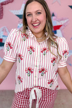 Load image into Gallery viewer, Woman wearing a red and white striped shirt with floral embroidery and red checkered pants against a pink background.