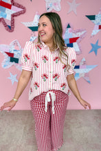 Load image into Gallery viewer, Woman wearing a red and white striped shirt with floral patterns and red checkered pants, standing against a pink wall with star decorations.