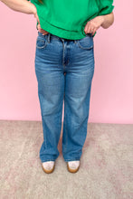 Load image into Gallery viewer, Person wearing a green top and blue jeans against a pink background