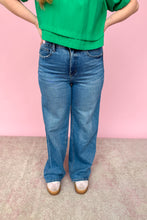 Load image into Gallery viewer, Person wearing a green top and blue jeans against a pink background