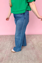 Load image into Gallery viewer, Person wearing blue jeans and a green top on a pink background side view