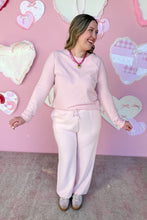 Load image into Gallery viewer, Woman in pink outfit standing in front of a heart-patterned wall.
