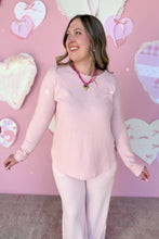 Load image into Gallery viewer, Woman wearing a pink sweater and pink pants against a pink background with heart decorations.
