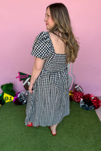 Load image into Gallery viewer, Girl wearing a black and white gingham midi dress with red jelly flats in front of a pink game day backdrop.
