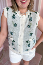 Load image into Gallery viewer, A woman wearing a cream-colored knit sleeveless vest with green and blue floral patterns, paired with white shorts.
