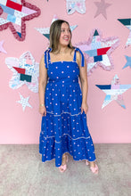 Load image into Gallery viewer, Woman in a blue dress with pink polka dots standing in front of a pink wall with star decorations.
