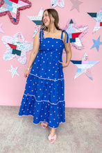 Load image into Gallery viewer, Woman in a blue dress with white polka dots standing in front of a pink wall with star decorations.

