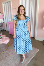 Load image into Gallery viewer, A woman wearing a light blue midi dress with dark blue polka dots, featuring puff sleeves and a square neckline, standing in a pink-themed room.
