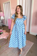 Load image into Gallery viewer, A woman wearing a light blue midi dress with dark blue polka dots, featuring puff sleeves and a square neckline, standing in a pink-themed room.
