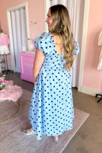 Load image into Gallery viewer, A woman wearing a light blue midi dress with dark blue polka dots, featuring puff sleeves and a square neckline, standing in a pink-themed room.
