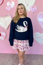 Load image into Gallery viewer, Woman wearing a navy sweater with a swan design in front of a pink wall with heart decorations.
