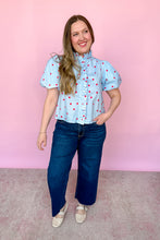 Load image into Gallery viewer, Girl wearing a blue top with red polkadots with puff sleeves and dark wash jeans standing in front of a pink background. 
