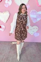 Load image into Gallery viewer, Woman in a floral dress with white blouse and boots standing against a pink heart-themed background
