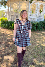 Load image into Gallery viewer, Girl wearing a brown and blue plaid skort and front tie top set with brown boots standing in front of a gazebo. 
