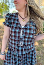 Load image into Gallery viewer, Girl wearing a brown and blue plaid skort and front tie top set with brown boots standing in front of a gazebo. 

