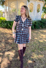 Load image into Gallery viewer, Girl wearing a brown and blue plaid skort and front tie top set with brown boots standing in front of a gazebo. 
