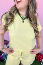 Load image into Gallery viewer, Girl wearing a yellow set with matching shorts and short sleeve top with a pink backdrop. 
