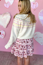 Load image into Gallery viewer, Woman wearing a cream sweater with floral patterns and a pink floral skirt against a pink heart-shaped background.
