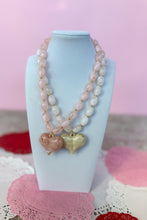 Load image into Gallery viewer, 2 Necklaces with heart-shaped charms on a white stand against a pink background
