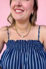 Load image into Gallery viewer, Woman wearing a blue striped dress with a pink background with a gold necklace stack
