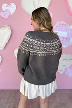 Load image into Gallery viewer, Person wearing a dark gray sweater with a pattern, standing against a pink wall with heart decorations.
