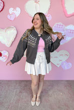 Load image into Gallery viewer, Woman in a posing in front of a pink wall with heart decorations in a gray cardigan with patterns 

