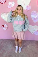 Load image into Gallery viewer, Person wearing a gray sweatshirt with 'PARIS' text and pink pleated skirt against a pink heart-patterned background.
