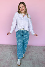 Load image into Gallery viewer, Woman wearing a lavender long-sleeve shirt and blue floral jeans against a pink wall.
